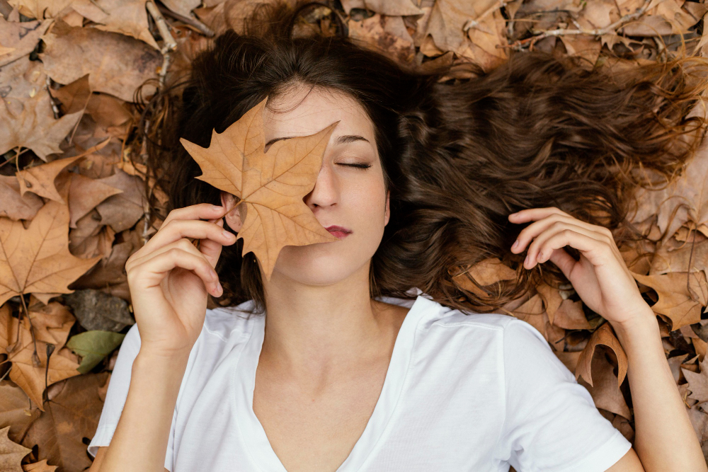 Chica en un bosque tumbada enseñando su cuidado para el pelo en otoño
